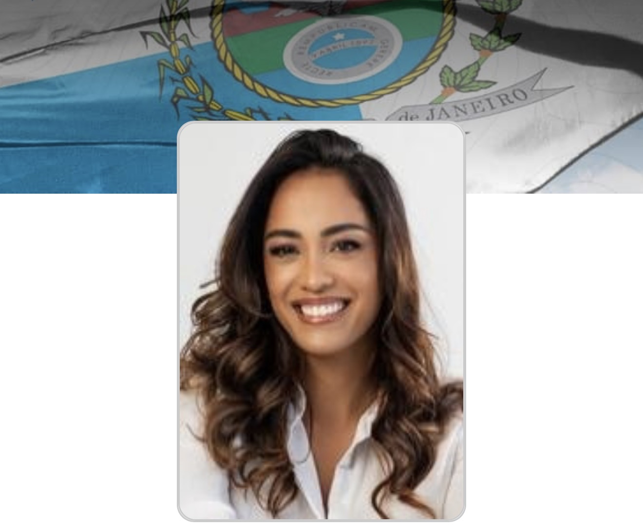 Ana Paula Mendes sorrindo, de camisa branca e cabelos ondulados, em imagem de divulgação sobre a bandeira do estado do Rio de Janeiro.